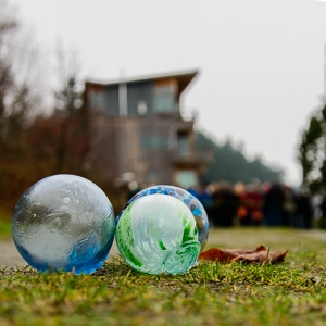 Three glass balls are on the ground with a crowd of people in the background behind a starting line.