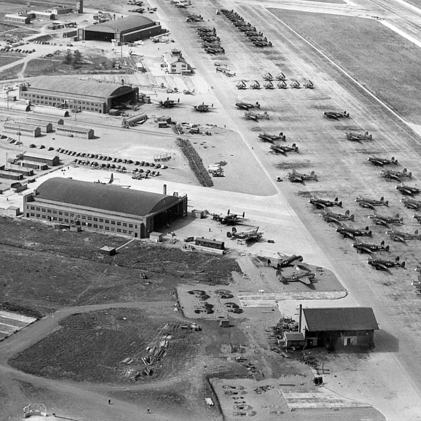 An aerial photo shows several hangers with several dozen airplanes parked outside.