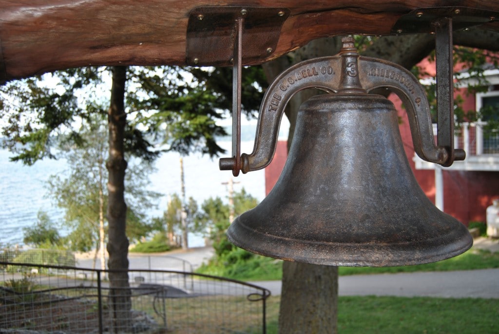 A large bell hangs from a wooden support in a park in Langley.
