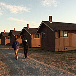 Two people walk among cabins built in the 1940's.