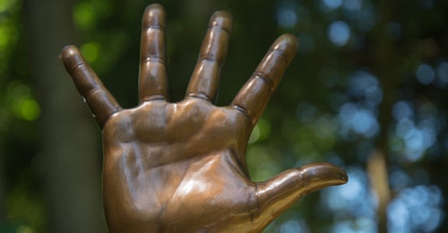 An open hand made of bronze is upraised.