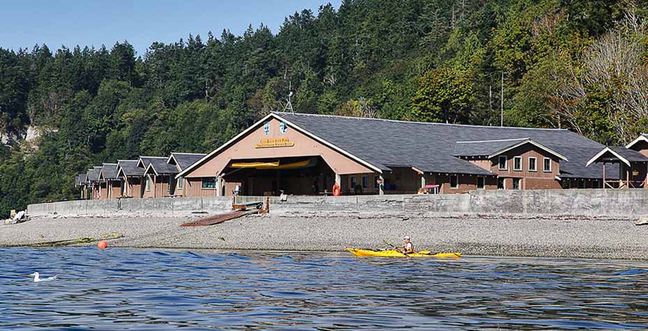 A large wood structure, the Center For Wooden Boats, is flanked by smaller buildings along the beach.