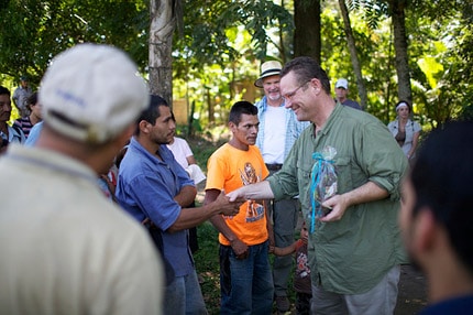 Jeff standing and talking with several farmers outside at a coffee bean farm.