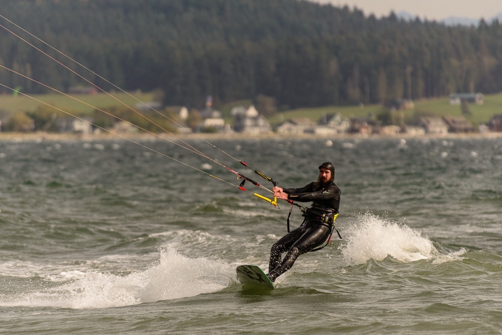 Man in a wet suit being pulled by a kite (not seen) while on a wave board.