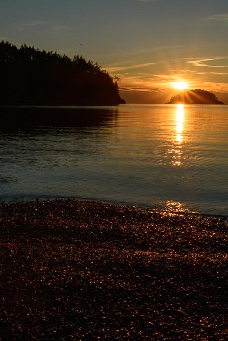 The sun is setting at Bowman Bay. The pebbled bach is in the foreground.