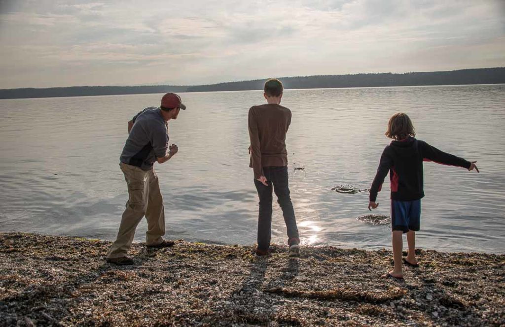 Three people skipping stones into the water