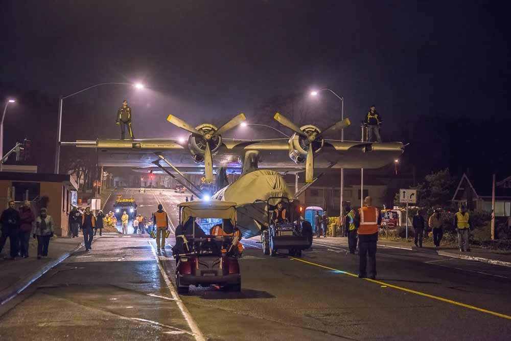 Airplane towed by a small tractor down a street at night.