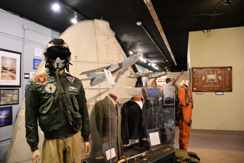 Mannequin dressed in a flight suit with helmet and smaller mannequins dressed in various Naval uniforms.