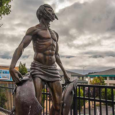 Statue of a Native American carrying a large salmon in each hand.