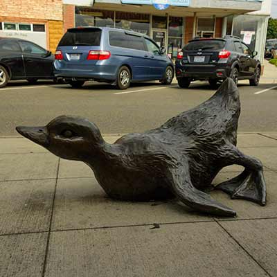 A large bronze duck has stumbled and landed on its chest.