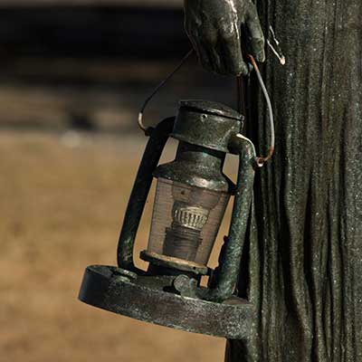 A bronze lantern in the hand of a woman statue.