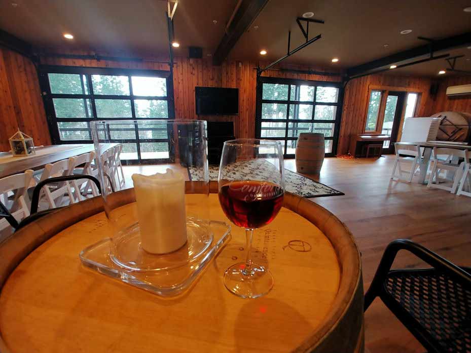 A glass of wine and a candle sit atop a wine barrel