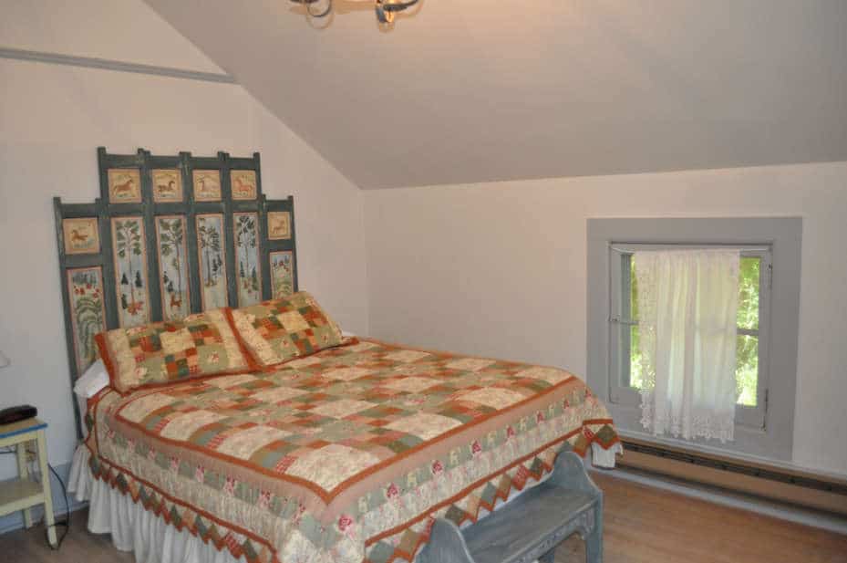 Qulted bedspread covers a double bed with an antique headboard painted with nature scenes.