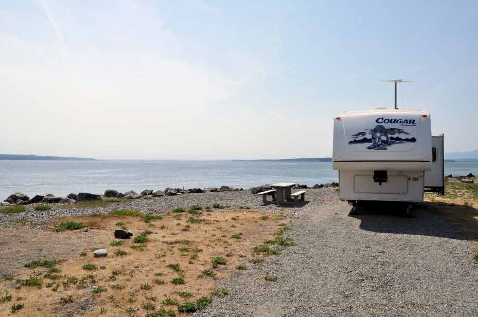 A camper in a parking spot with a picnic table and Admiralty Inlet in the background.