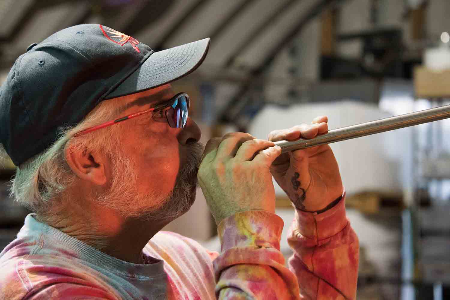 Man blowing into a glass making pipe.