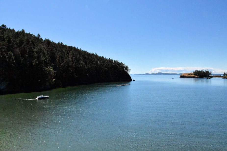 The waters of Bowman Bay with a boat in the water and part of Fidalgo Island, densely packed with trees, in the background.