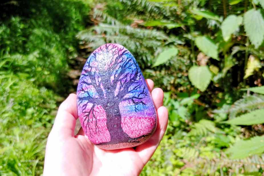 A hand holding a smooth rock and a tree is painted on it