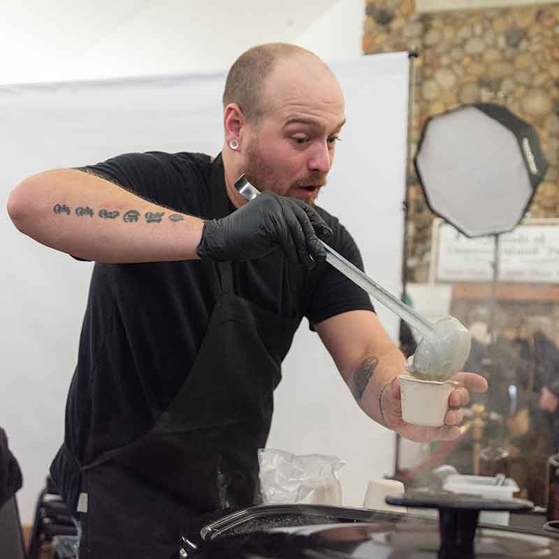 Man using a ladle to put chowder in a paper cup.