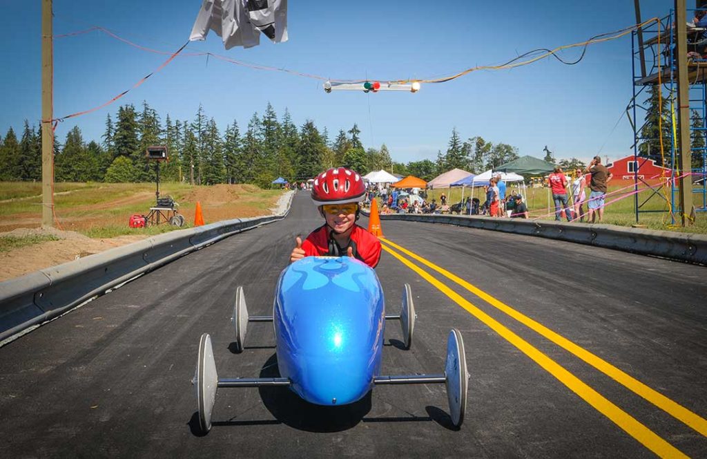 Young boy in a helmet in a blue gravity-powered race car.