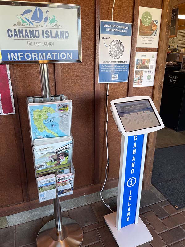 Computer on a stand along with a rack of printed visitor guides and maps