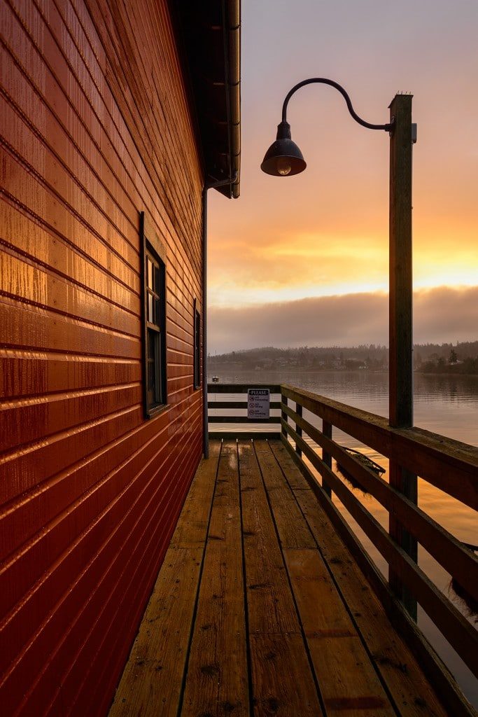 The red walls of the Coupeville Wharf are backed by the oranges of a sunrise.