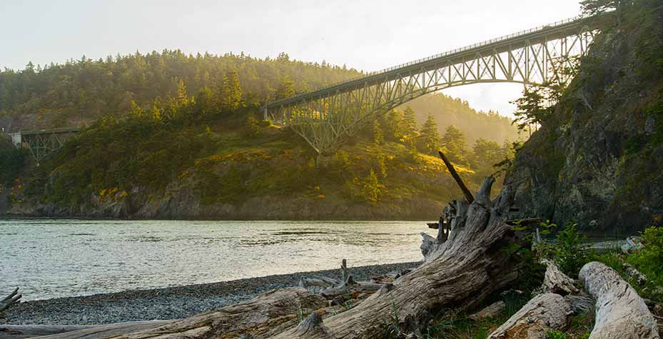 The Deception Pass Bridge towers over the beach as the morning sun lights the bridge from behind.