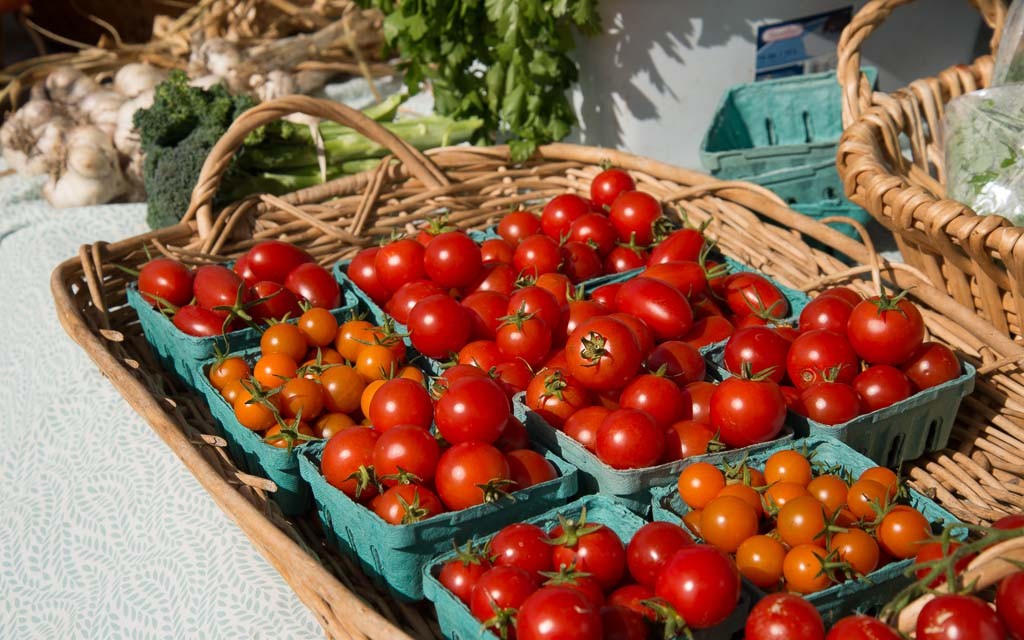 Several containers of cherry tomatoes are sitting in a wicker basket.