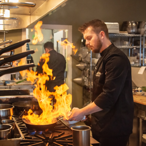 Chef at a stove and whatever he's cooking is flaming up.