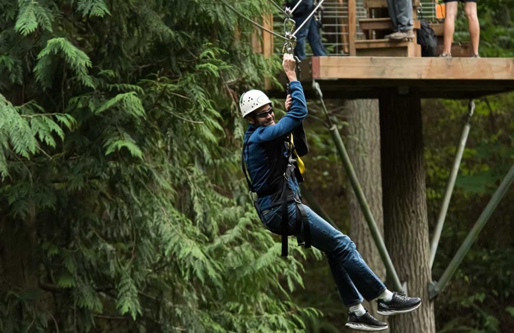 Man in a helmet is strapped into a harness and sliding down a zip line.