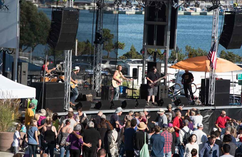 A band is on a stage with people dancing in front of the stage.  There is the  water of Oak Harbor in the background.