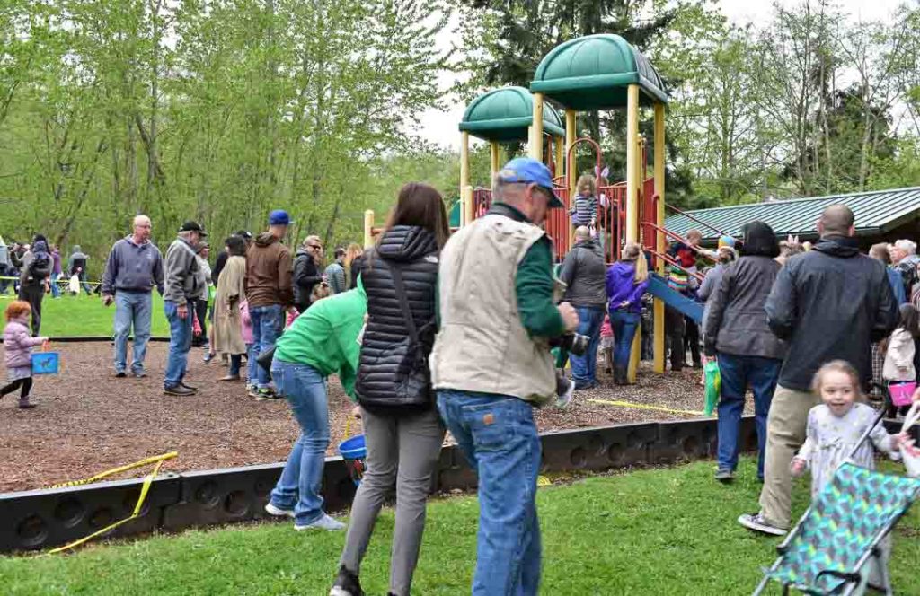 Kids hunting for Easter Eggs in a playground and adults are watching them.