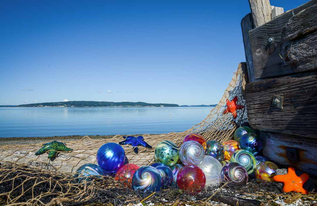 A dozen colorful glass fishing floats and sea stars resting on a fishing net on a beach