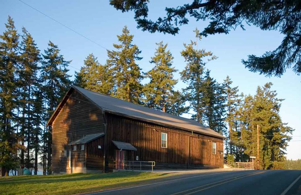 An old wooden barn-shaped building surrounded by trees.