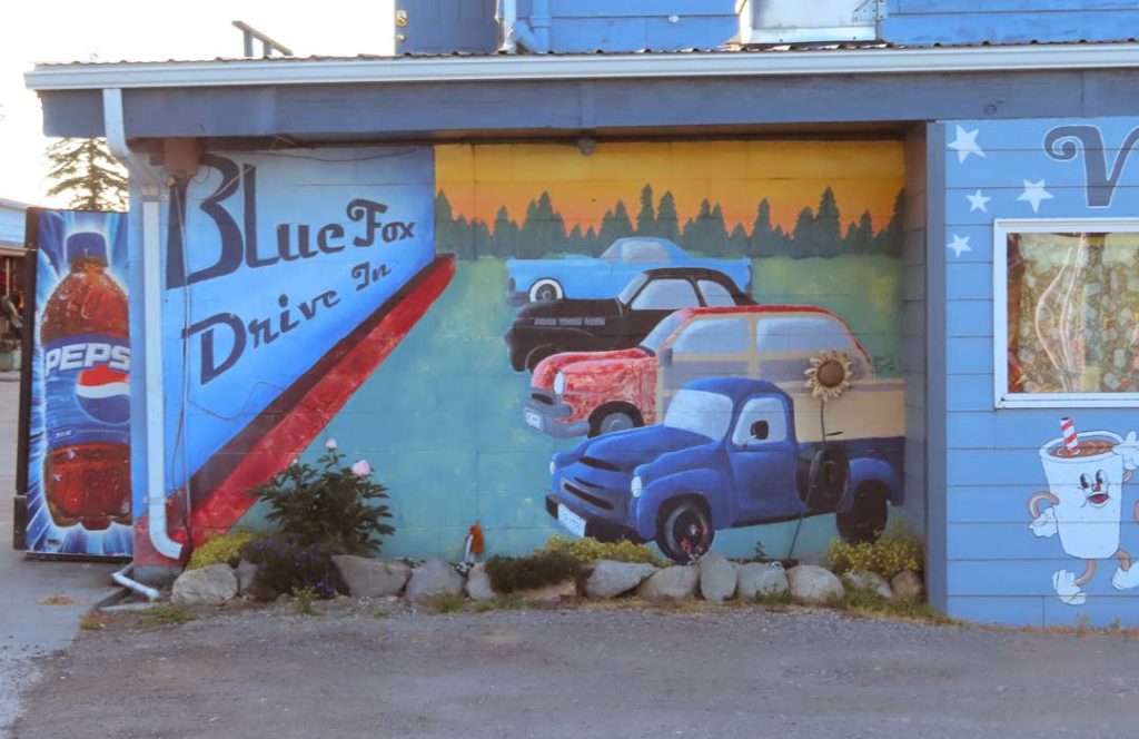 A mural of parked cars at a drive-in is on the side of the building.