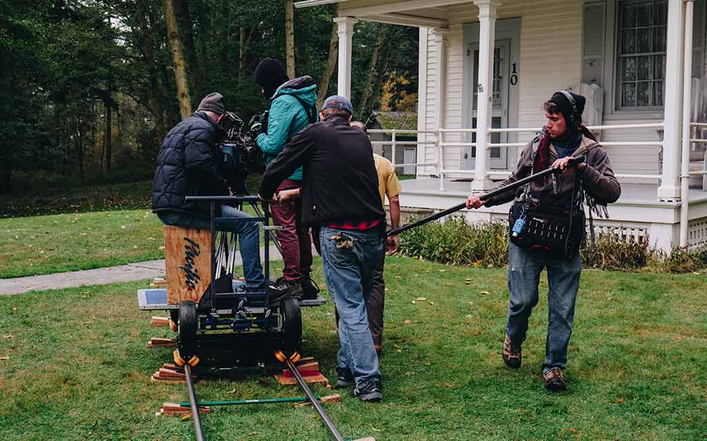 A film crew with a large camera on a dolly that is on portable tracks.