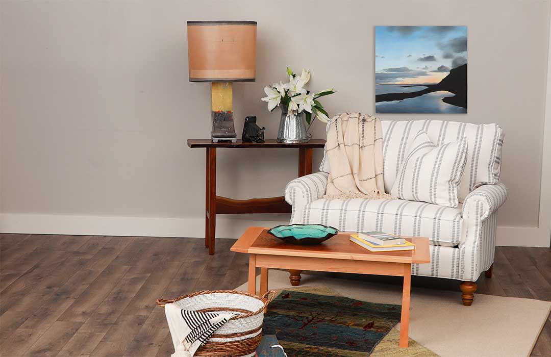 An artistically decorated living room with chair, lamp, coffee table, and painting.