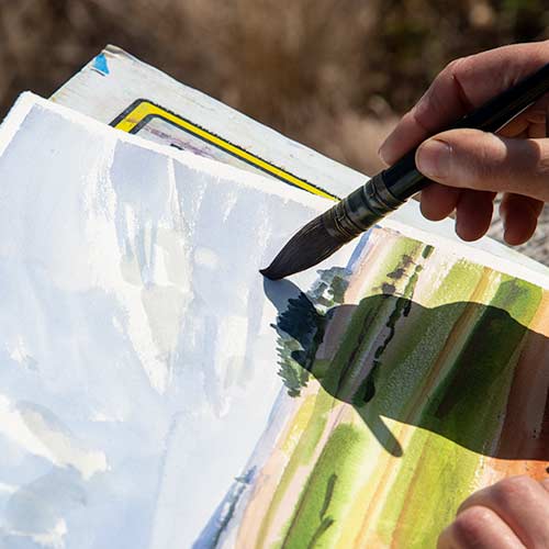 Hand holding a brush painting a watercolor.