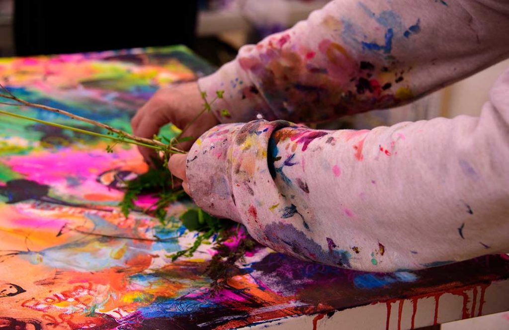 Close view of a painter's arms and hands.  The sweatshirt is stained with a collage of various colors of paint.