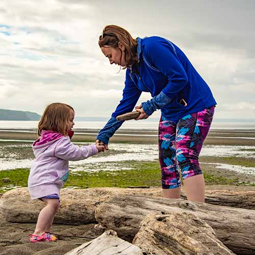 Mother helping young daughter step over driftwood