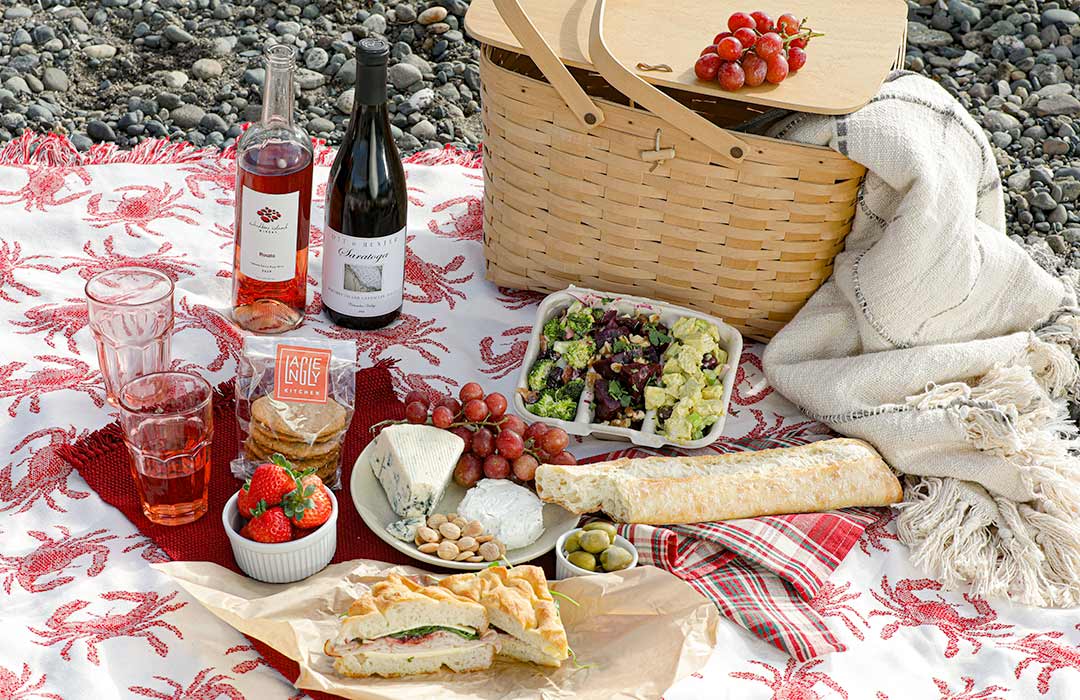 Picnic Basket, bottles of wine, cheese and frut all spread out on a blanket