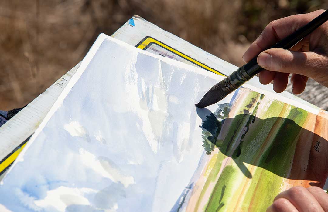 hand holding a paintbrush painting a watercolor