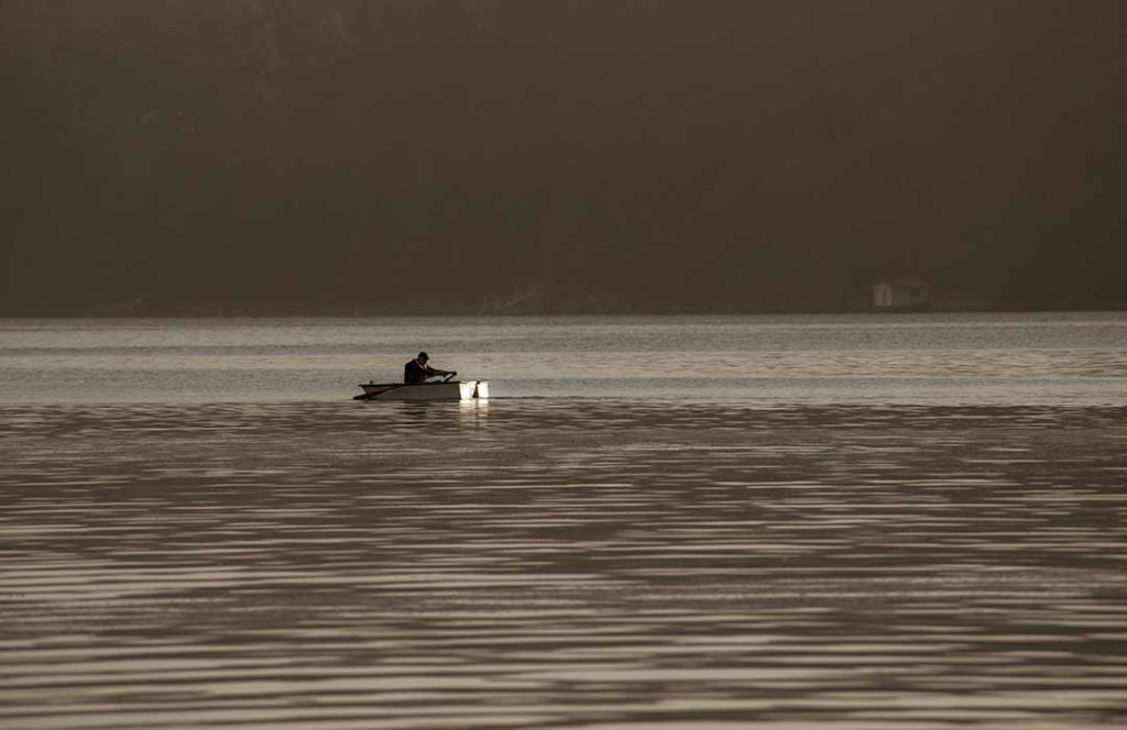 Lone man in a small rowboat several hundred yards off shore