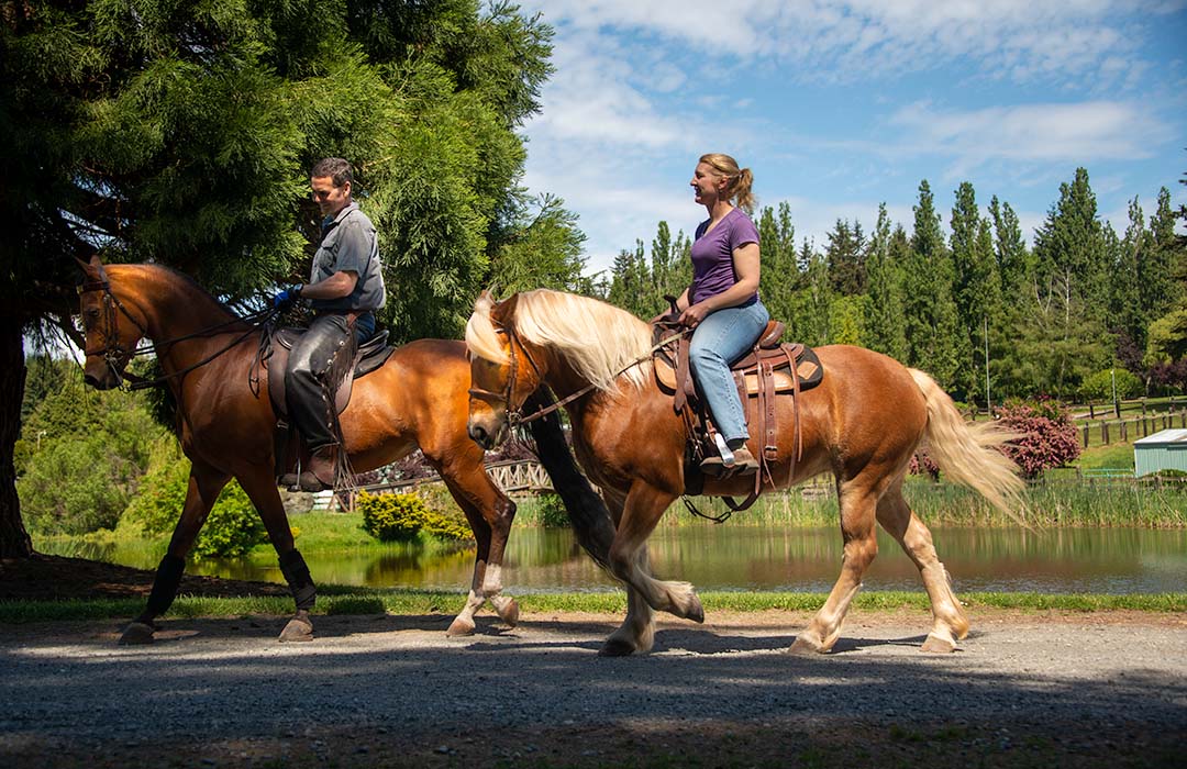 A man and woman riding horses past a lake.