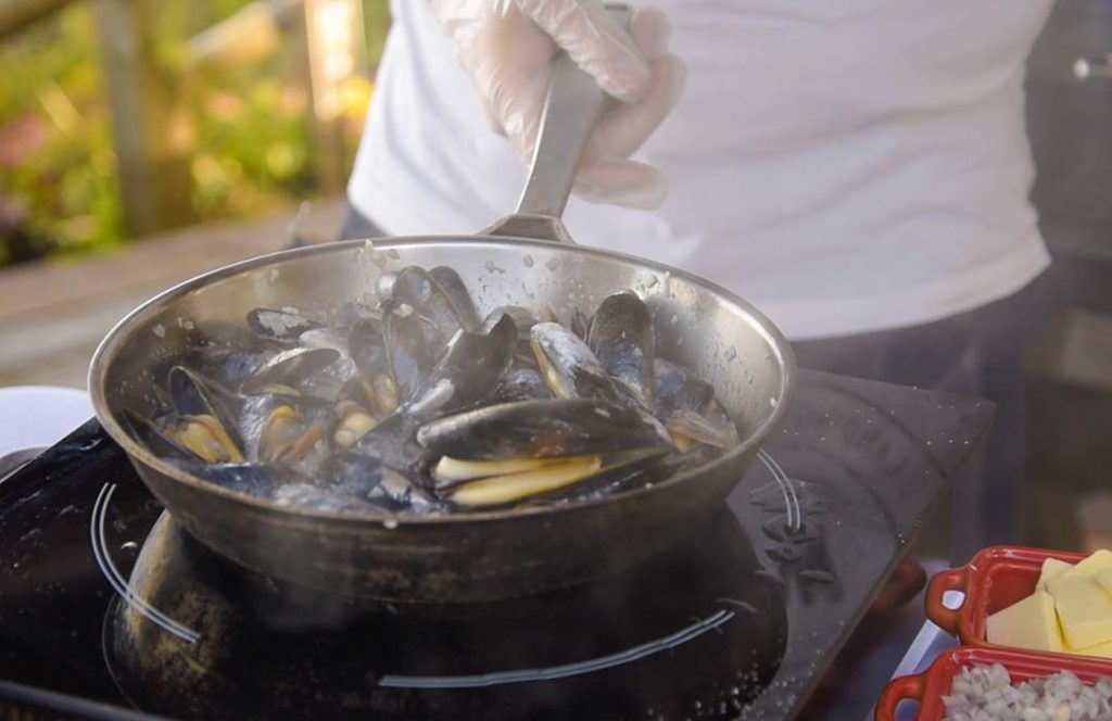 Metal pan filled with mussels being cooked on an induction burner.