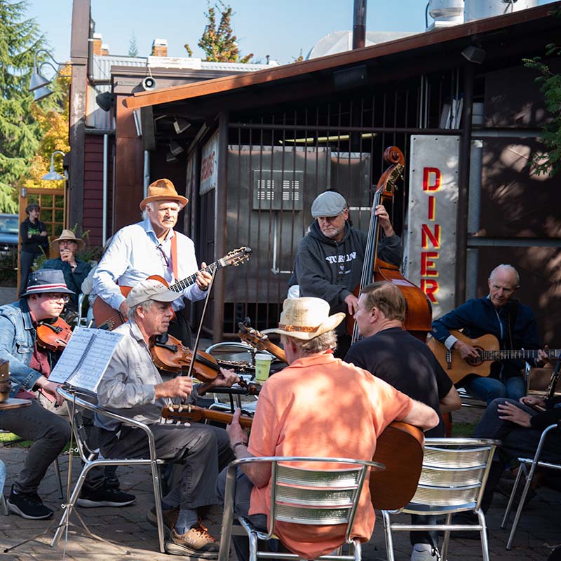 Musicians gathered around an outdoor table playing music.