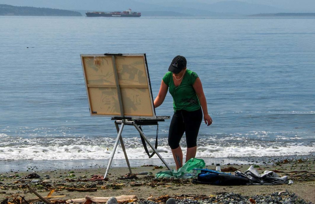 Woman at an easel painting. She's on a beach.