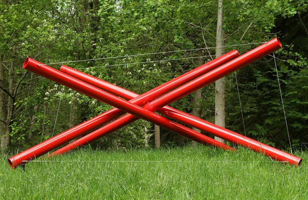 Four large red pipes at various angles are held in place by wires and the crisscrossing of the pipes.