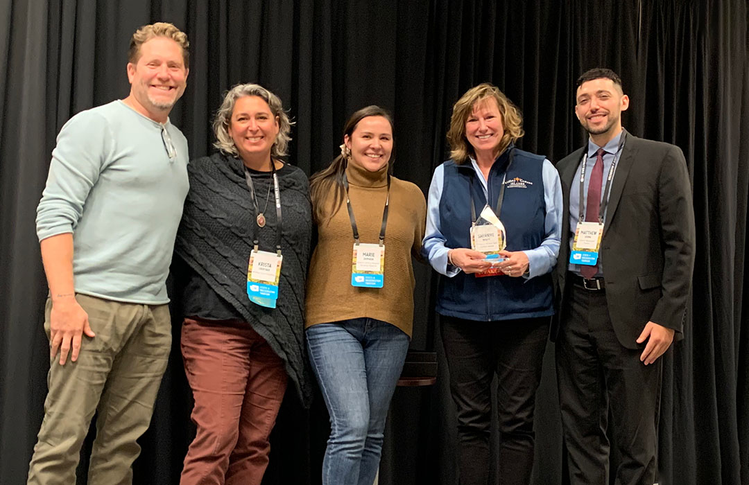 Five people posing for the camera and one is holding a glass award.