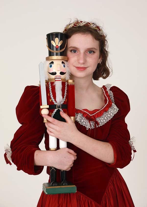 Young ballet dancer dressed in red holding a wooden nutcracker designed to look like a soldier.