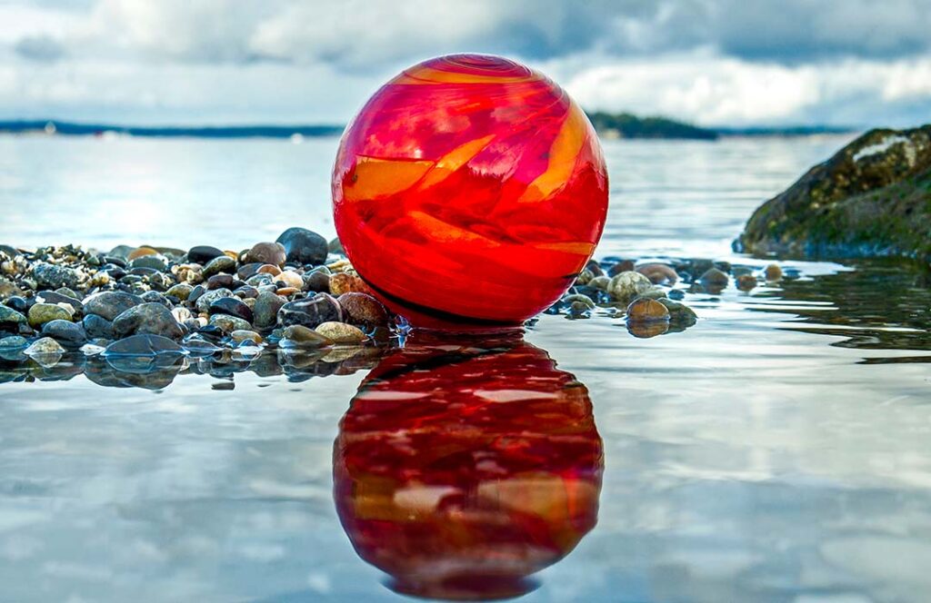 A red glass ball sits in shallow sea water.